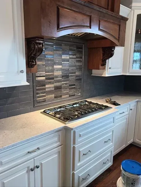 Kitchen with white cabinets, gray countertop, and stove, with a dark wooden range hood.