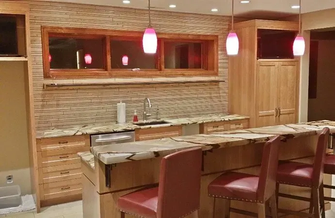 Bar with wood cabinets, granite countertops, red stools, and pink pendant lights.