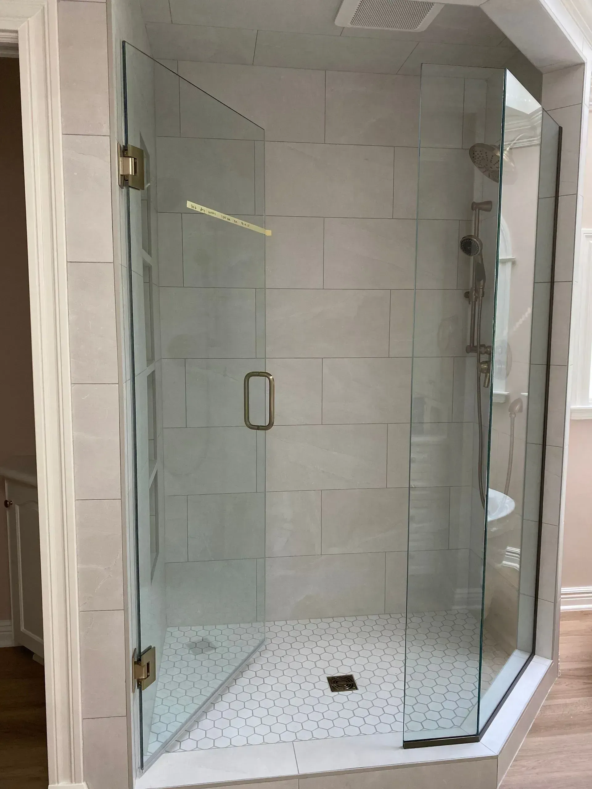 Frameless glass shower enclosure with white tile walls and speckled floor.