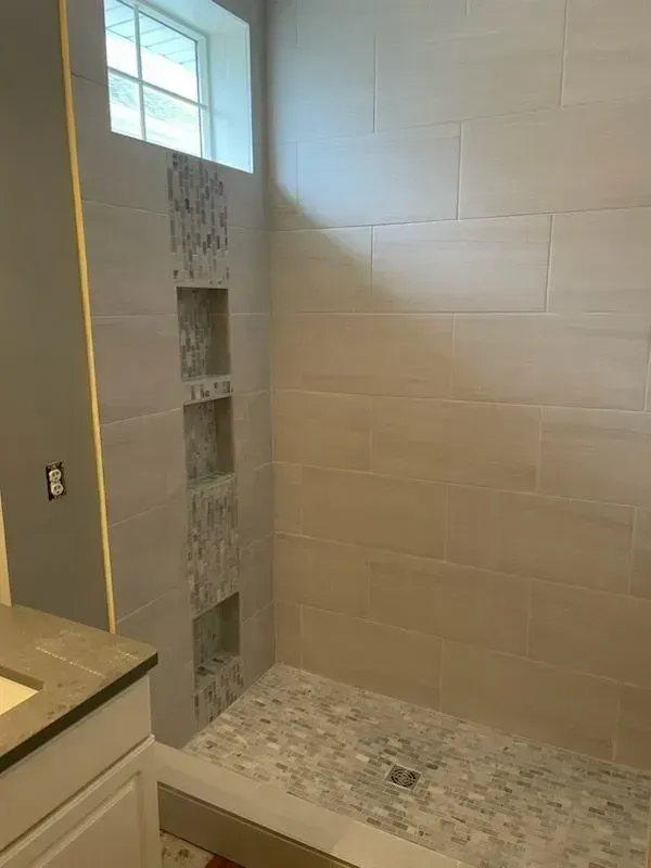 Bathroom with gray tiled shower, pebble shower floor, and built-in niches with patterned tile accents.