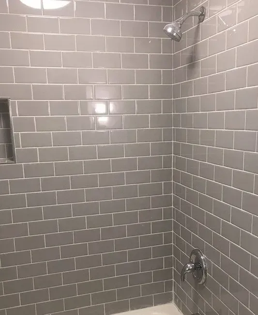 Gray tiled shower with showerhead, faucet, and built-in shelf.