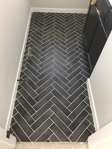 Dark gray herringbone tile flooring in a hallway with white trim and dark cabinets.