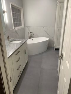 Modern bathroom with white vanity, soaking tub, and gray tile flooring.
