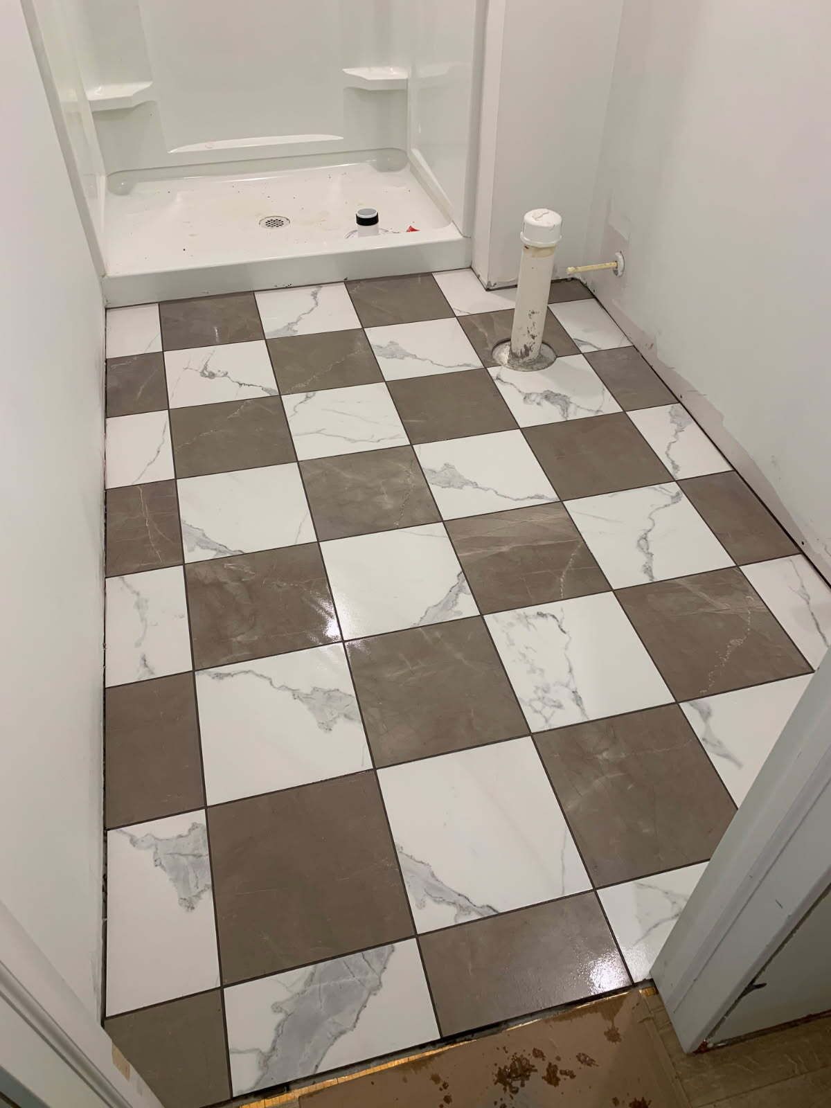 Bathroom floor with checkerboard pattern tiles, white shower stall, and exposed plumbing.