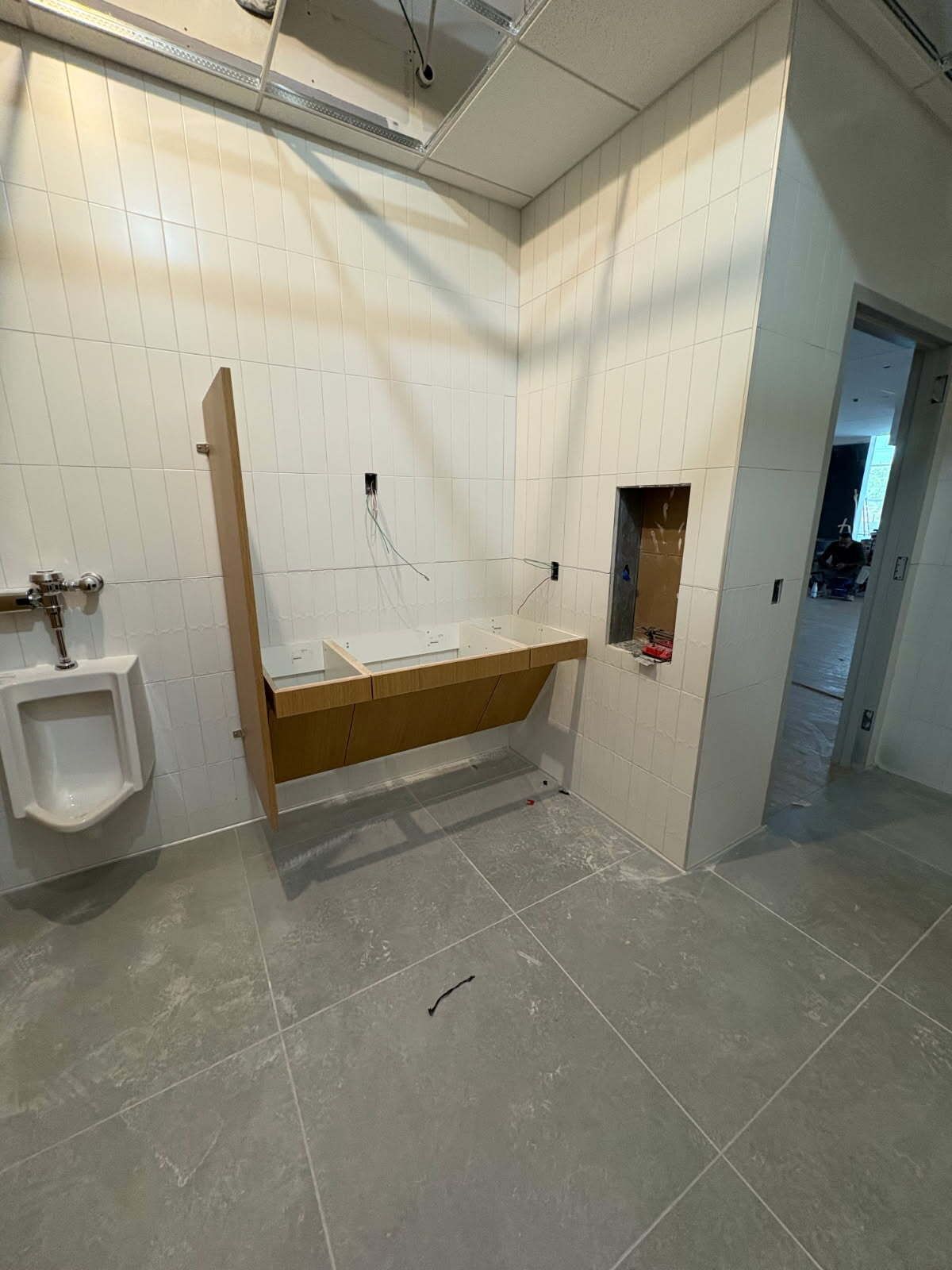 Construction of a handicap accessible bathroom. A white urinal, a wood counter, and a doorway.