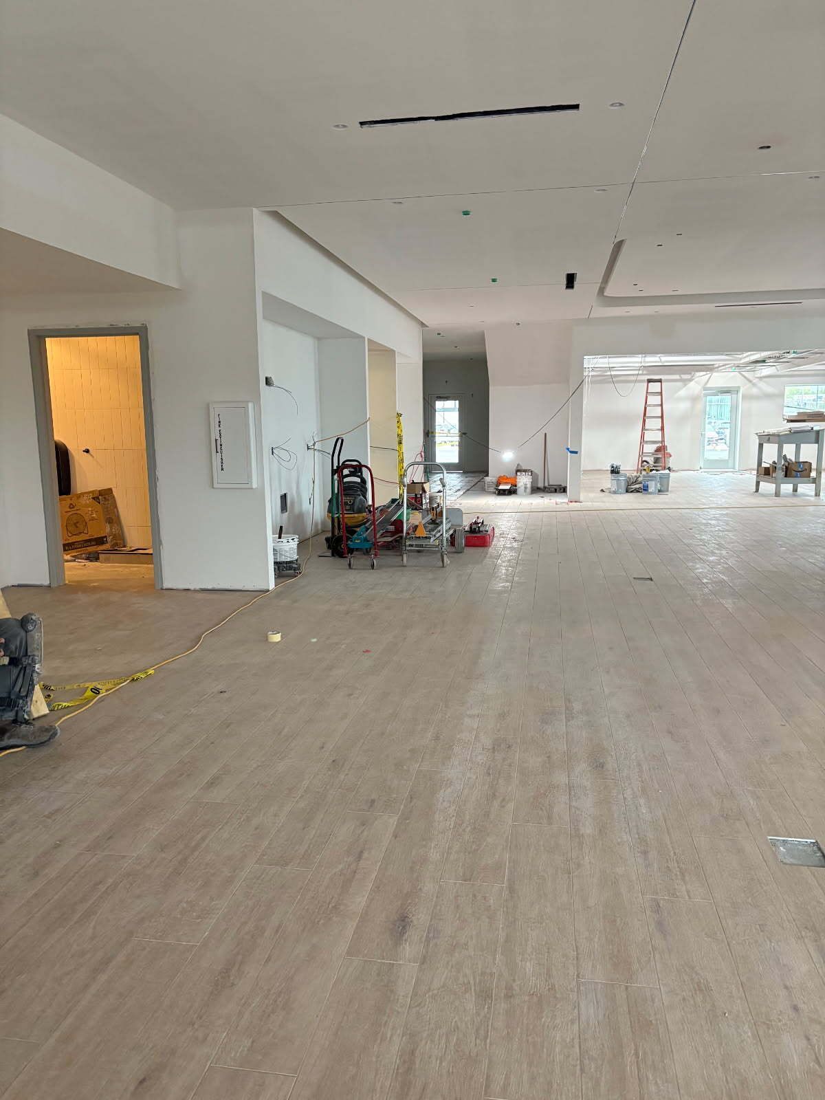 Open-plan room under construction; light wood floors, white walls, tools, and doorways.
