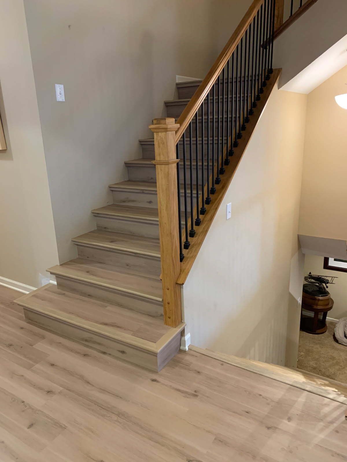 Staircase with light wood steps and flooring, black metal railing, and oak newel post.