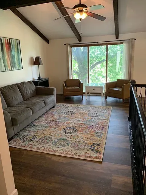 Living room with a sofa, chairs, and rug, with a large window overlooking trees.