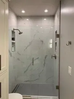 A modern marble-tiled shower with glass doors, recessed shelves, and silver fixtures.