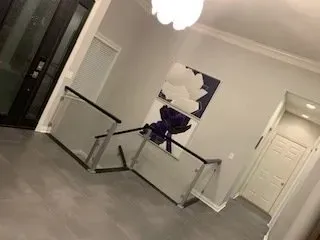 Interior view of a hallway with a glass railing, gray floors, and a floral painting.