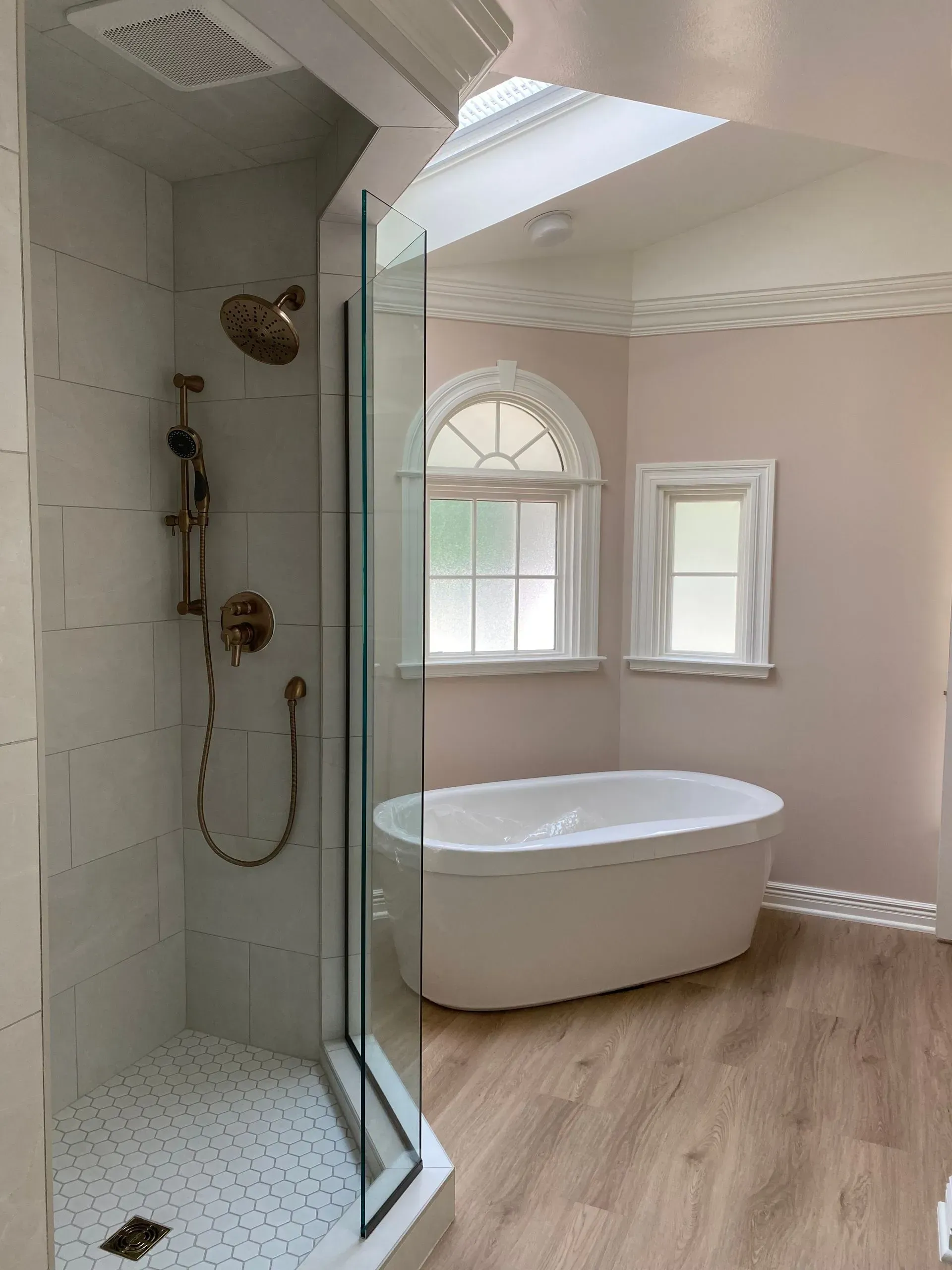 Bathroom with a shower, soaking tub, and two windows. Soft pink walls, light wood floors, and a skylight.