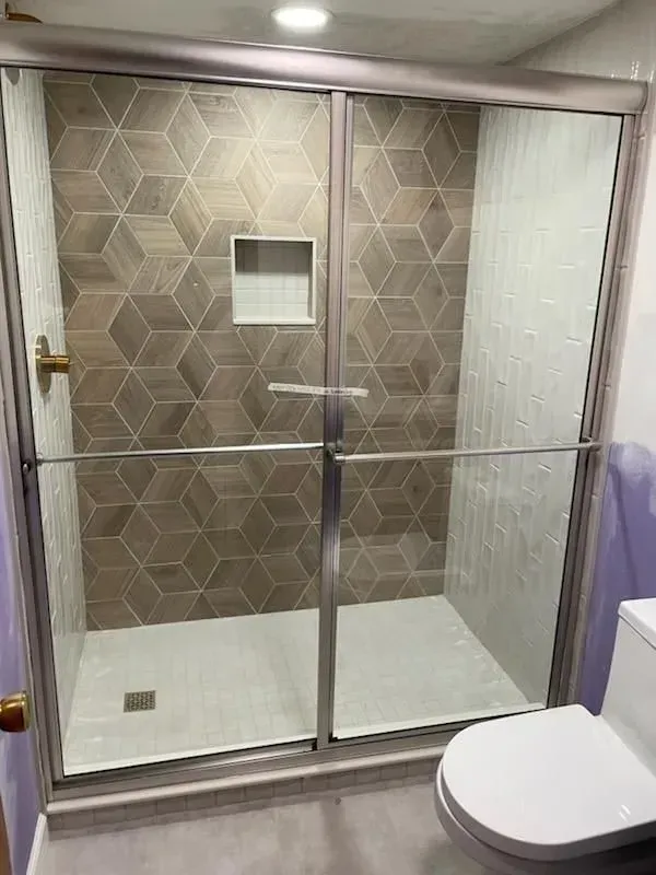 Shower stall with glass doors, tile walls, and a toilet on the right.