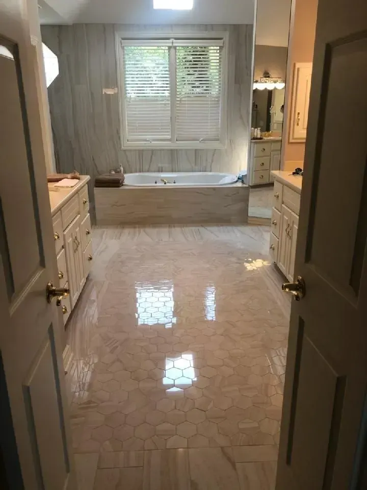 A large, bright bathroom with marble-look tile floors and walls, a soaking tub, and two vanities.