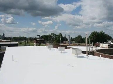 White flat rooftop with vents and pipes under a cloudy sky