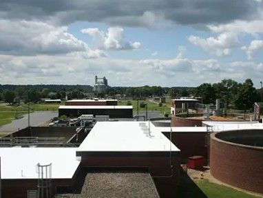 Rooftop view of industrial buildings under a cloudy sky, with trees and a distant silo in the background