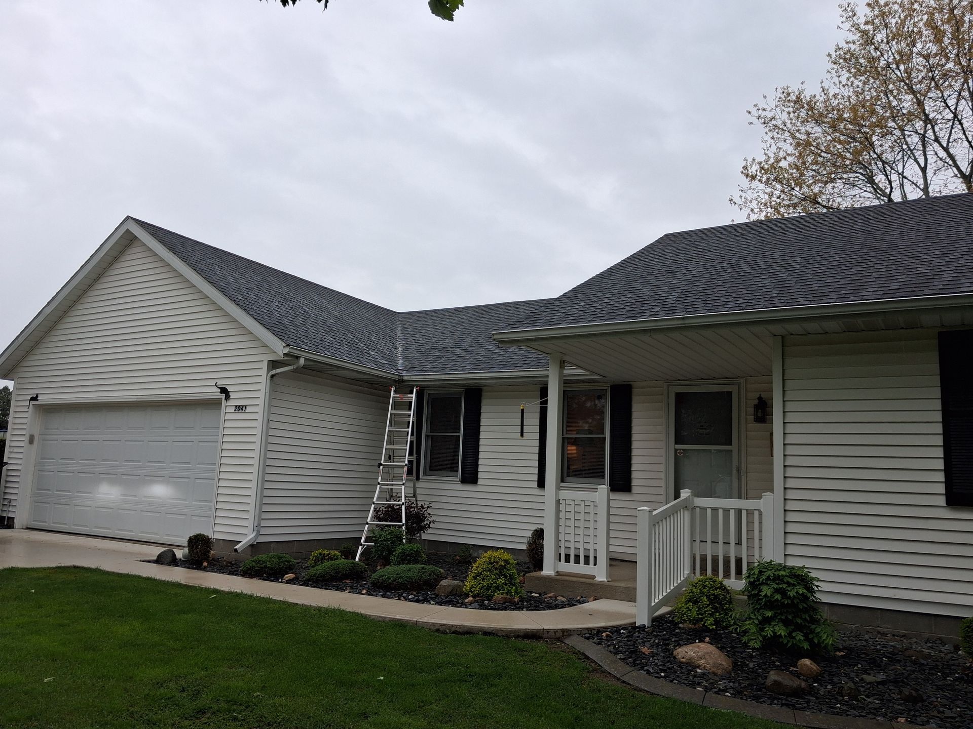 Suburban house exterior with white siding, attached garage, and small front porch under cloudy skies