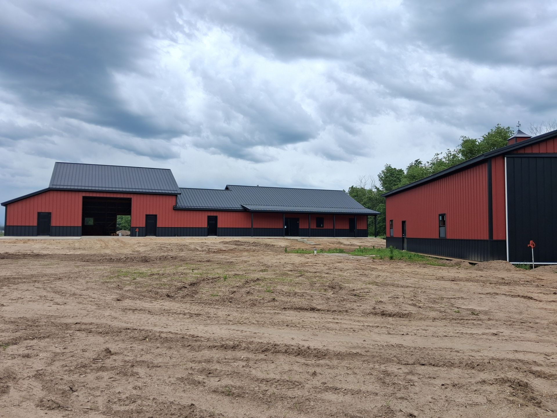 Red barn-style buildings on a muddy farmyard under a cloudy sky