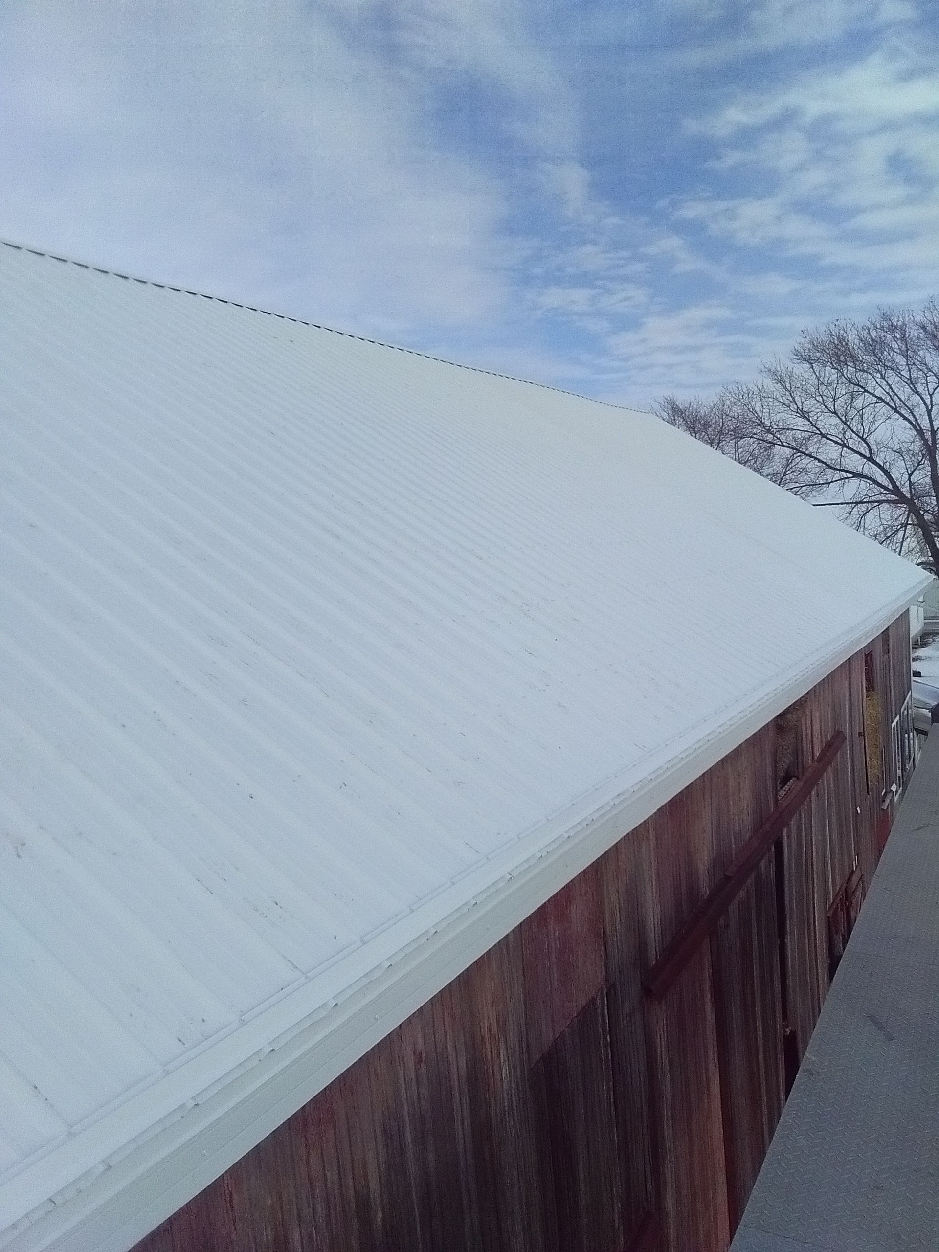 Snow-covered roof beside weathered wooden siding under a cloudy sky