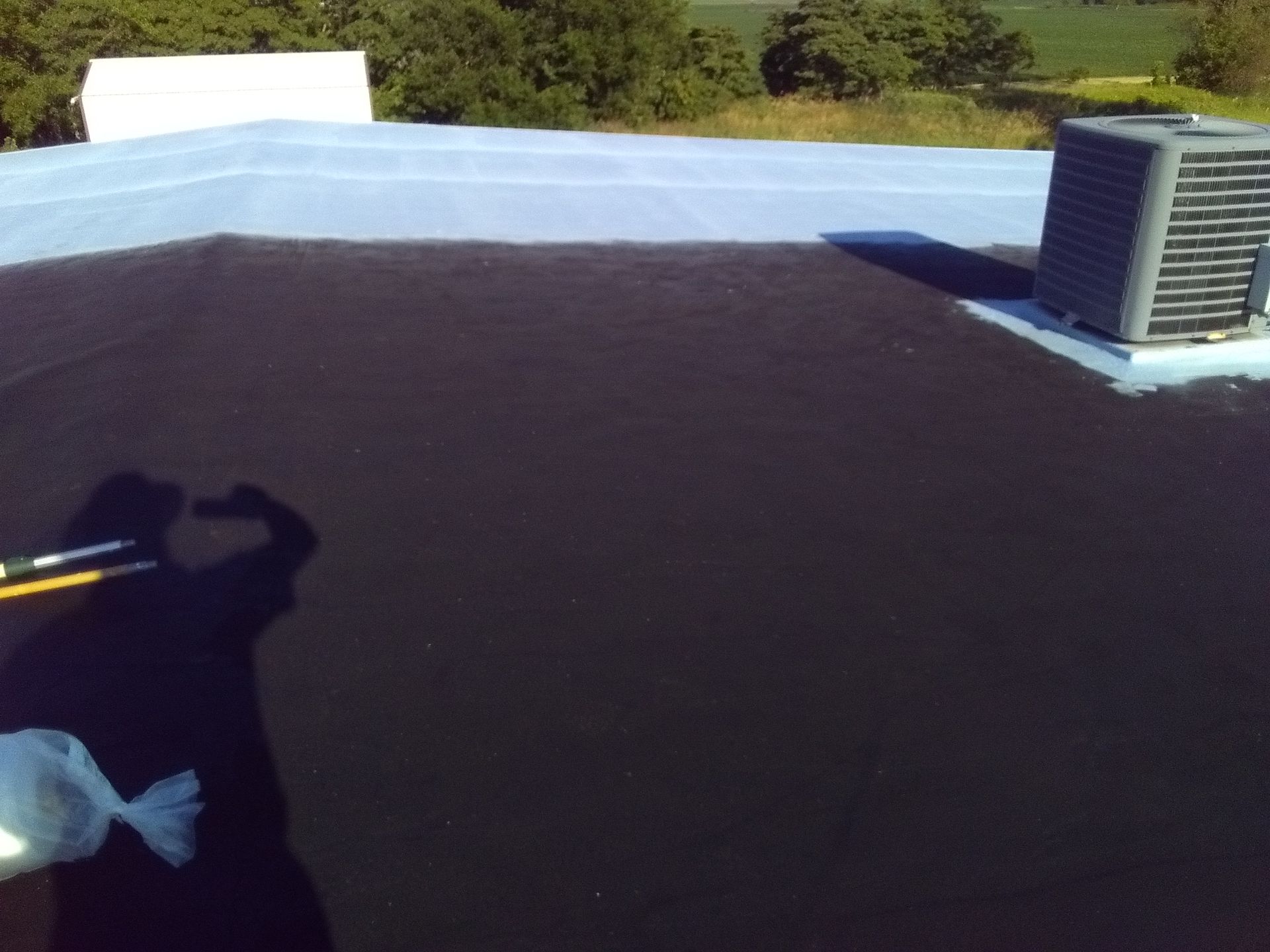 Flat rooftop with dark surface, blue parapet, and an HVAC unit on the right.