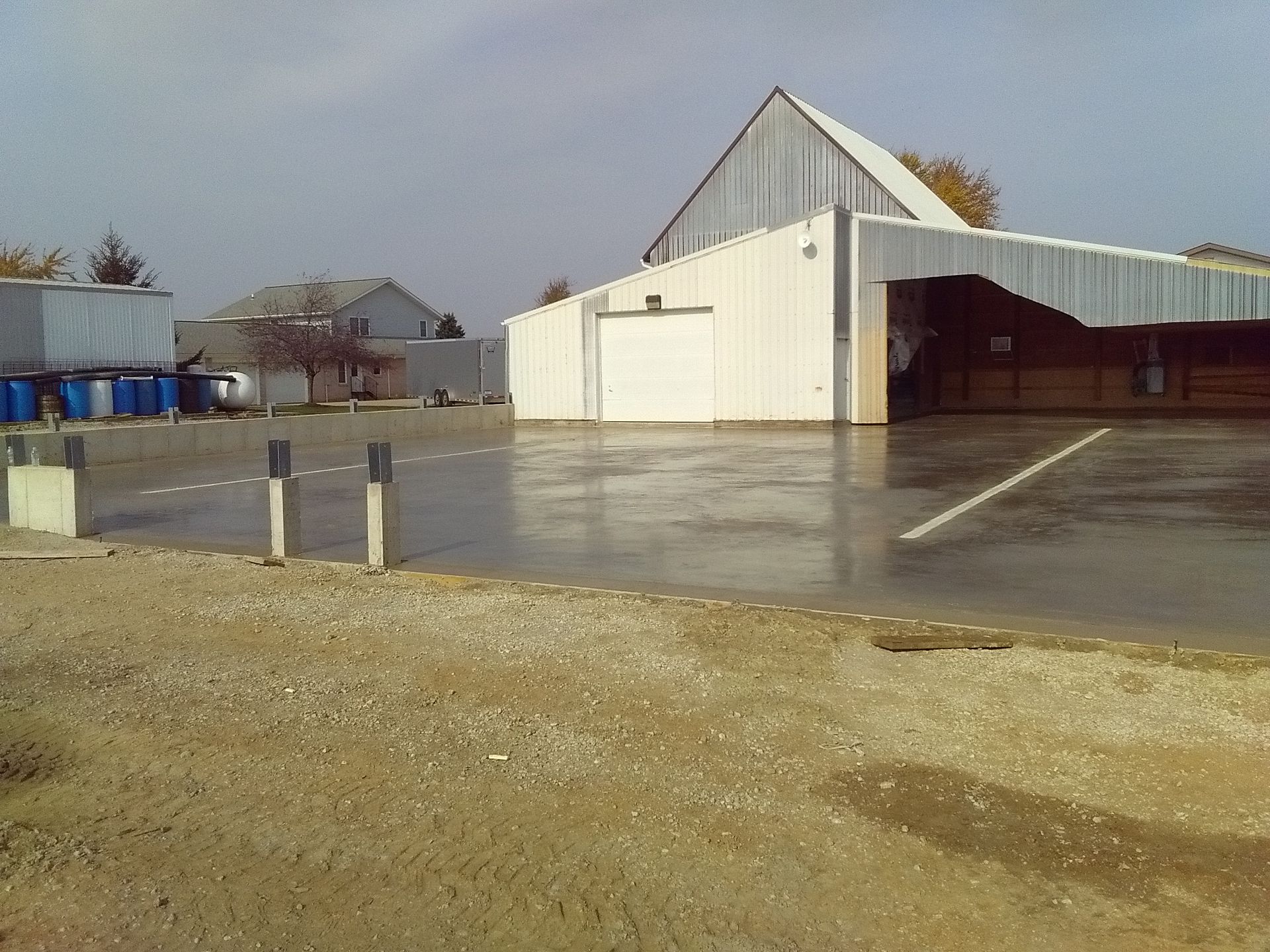 Rainy farmyard with a barn, metal buildings, and wet pavement under an overcast sky