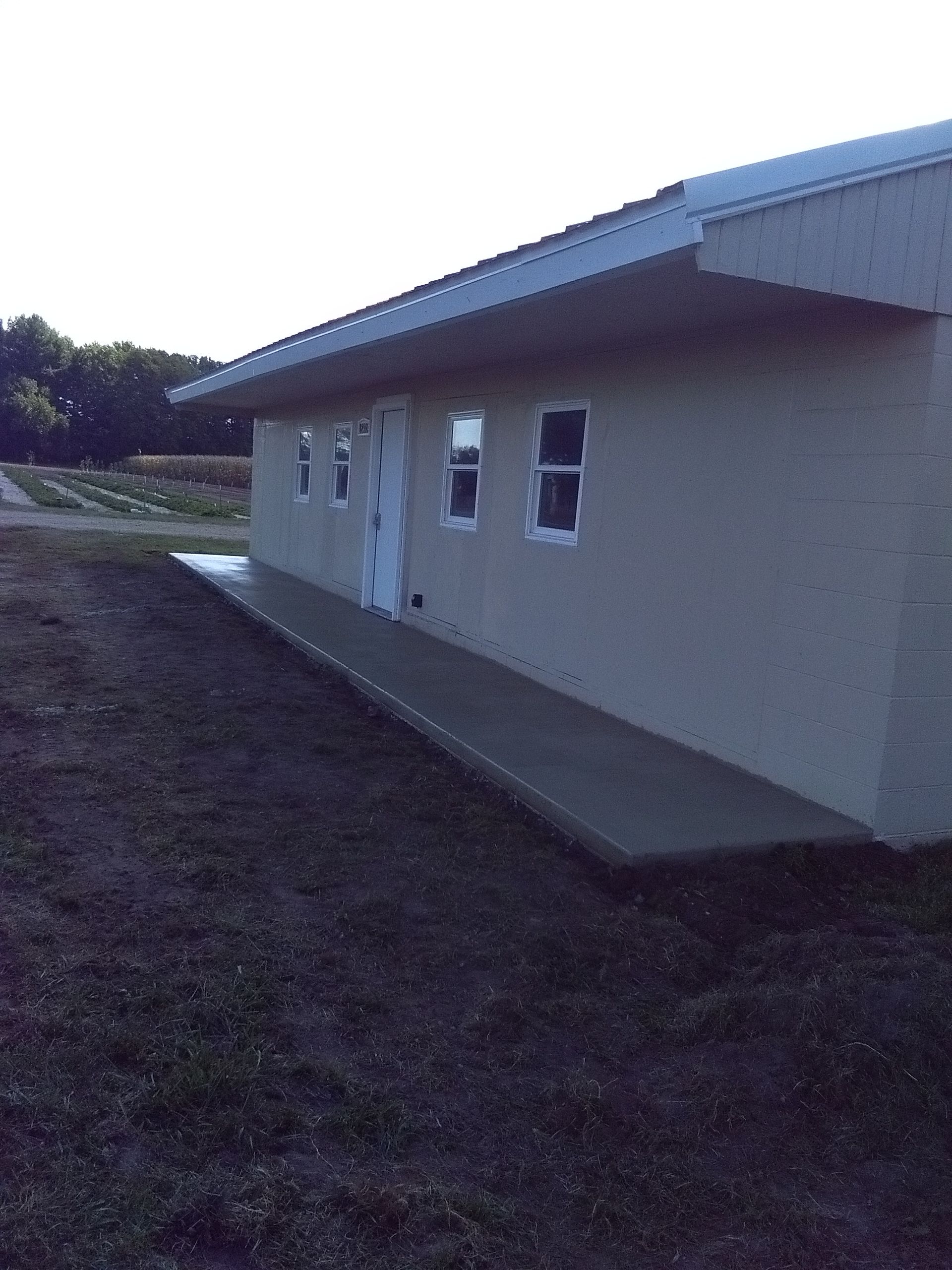 Side view of a beige building with windows, a sloped roof, and a concrete walkway beside it.