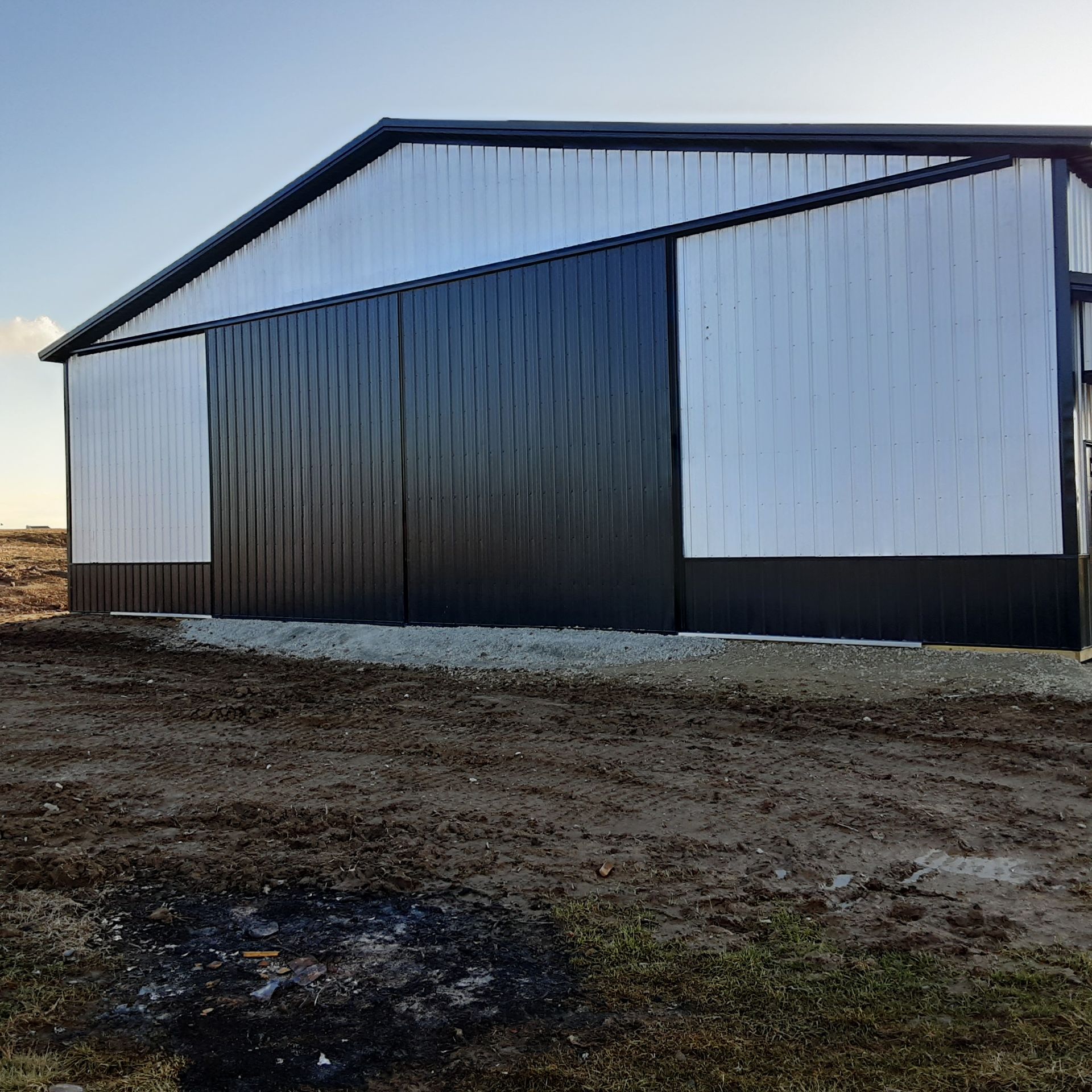 Large white and dark metal barn or storage building on a dirt lot at sunset