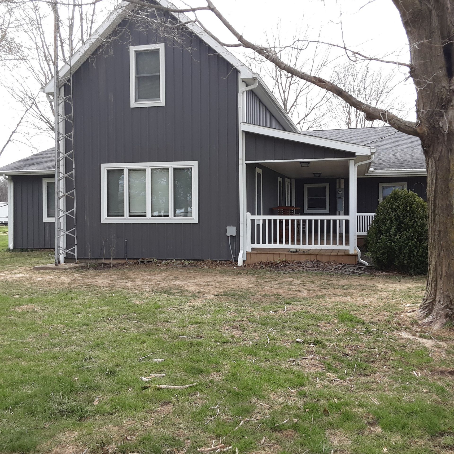 Gray two-story house with white trim, front porch, and ladder beside the side wall, viewed from a grassy yard