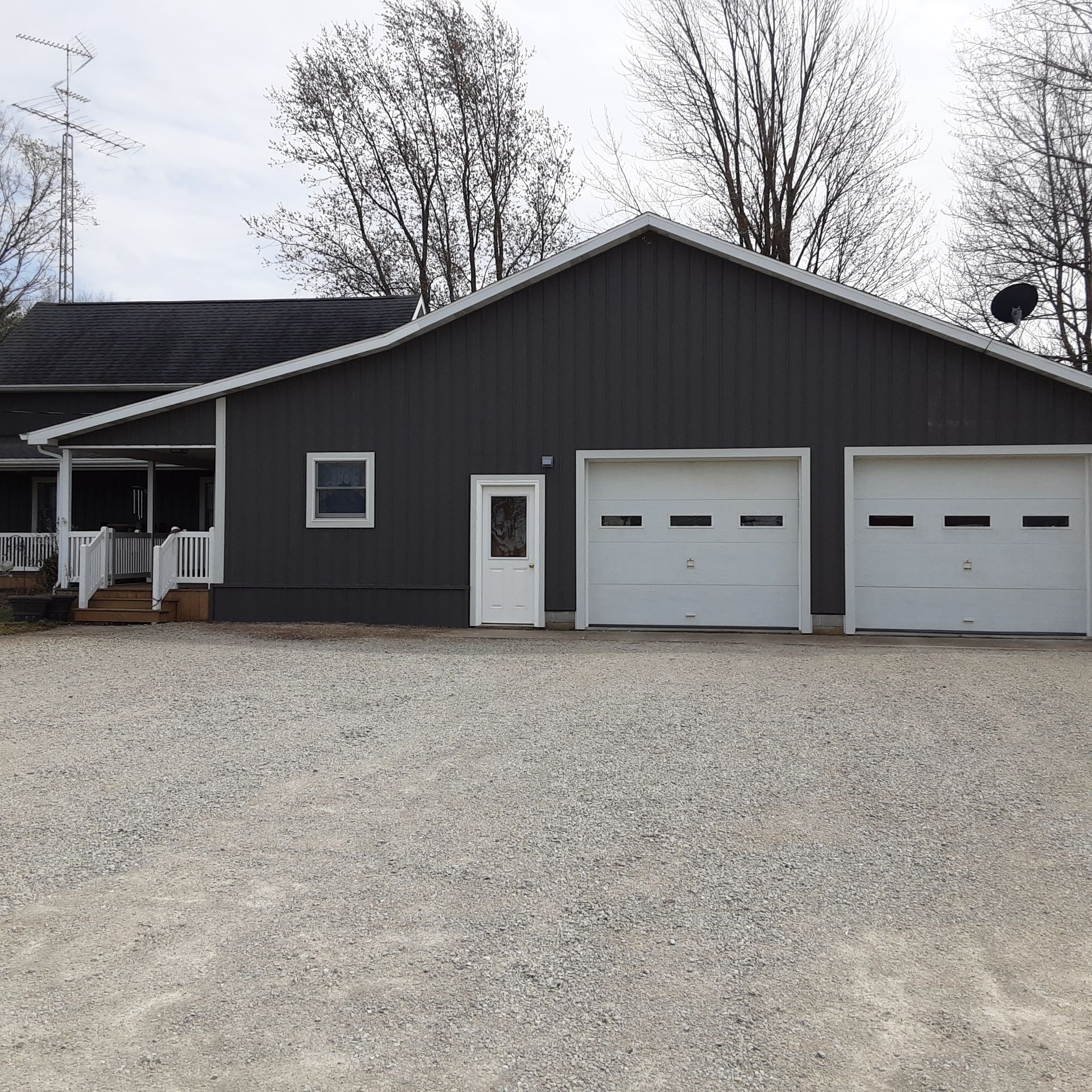 Gray house with two white garage doors, small porch, and gravel driveway under bare trees