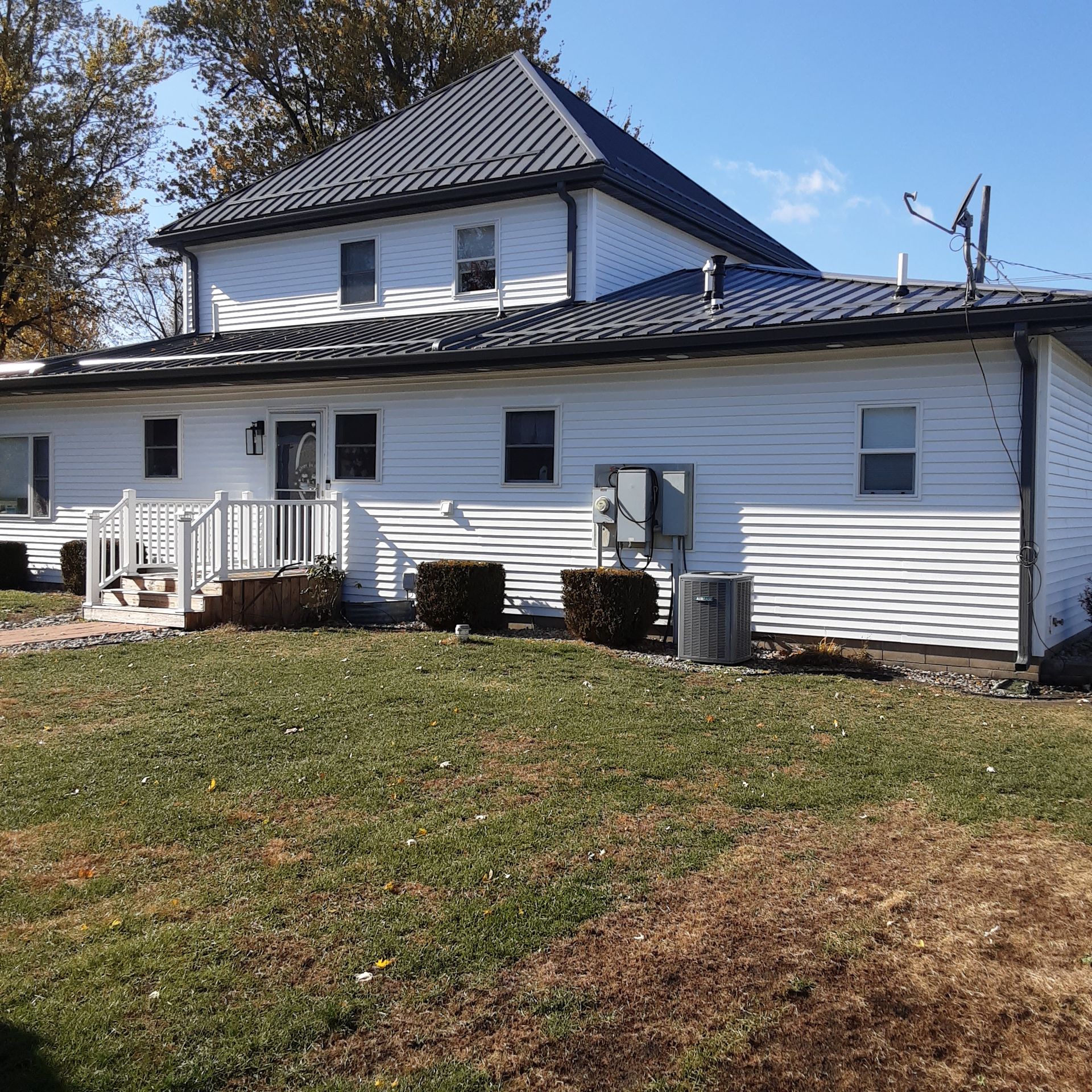 White house with dark roof and small porch on a grassy lawn under a clear sky.