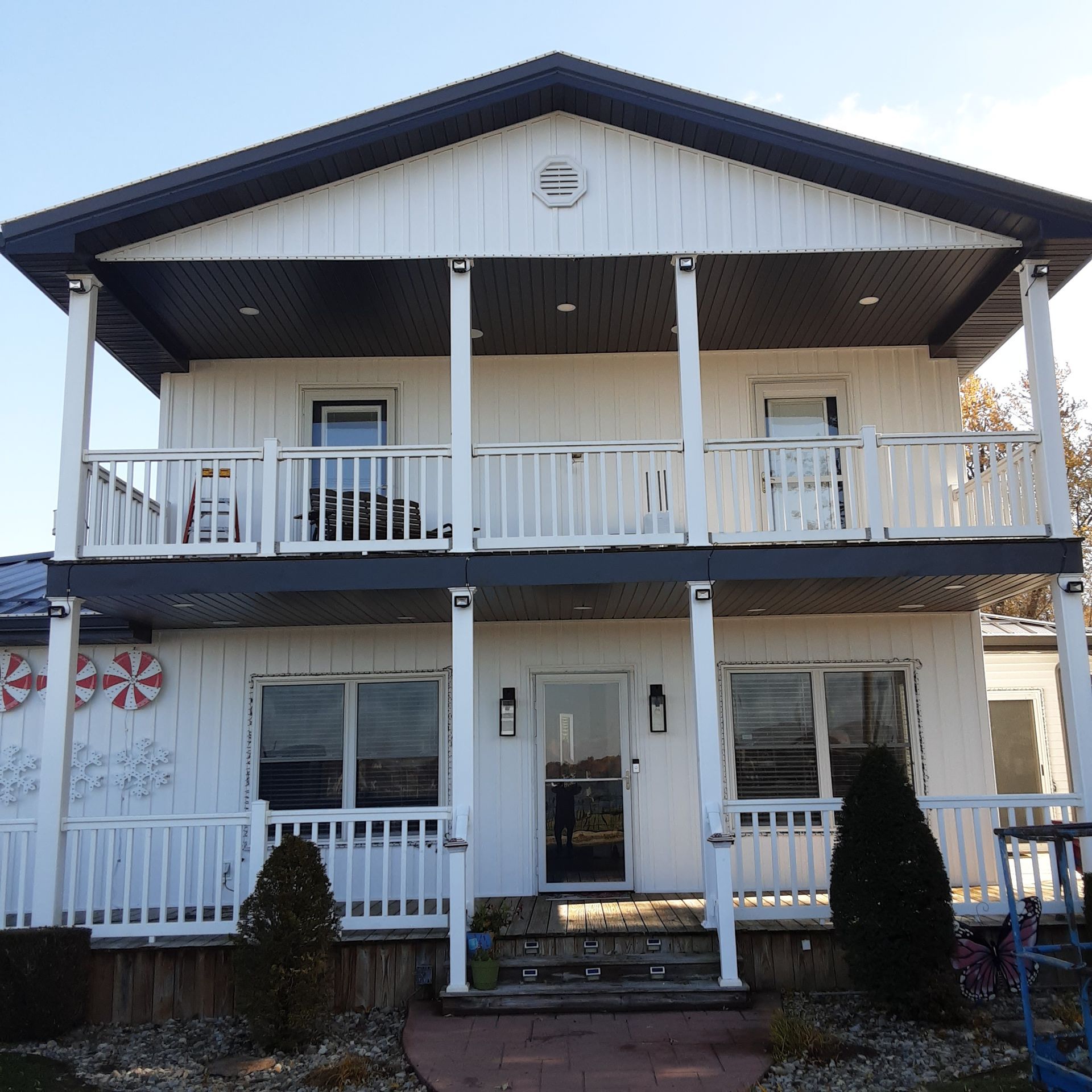 Two-story white house with wraparound porch, black roof, and front steps