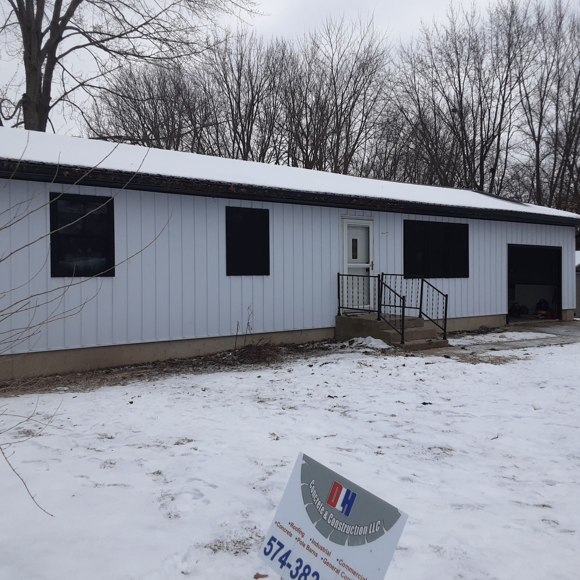 Snowy white building with black trim and a ramp, set against bare winter trees.