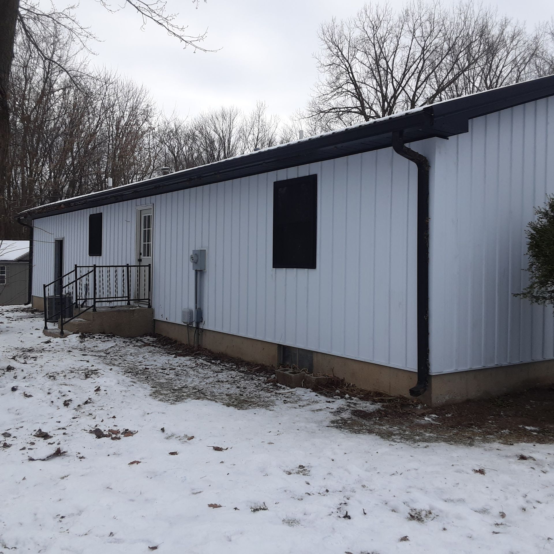 White modular house with black trim and snowy yard under bare winter trees