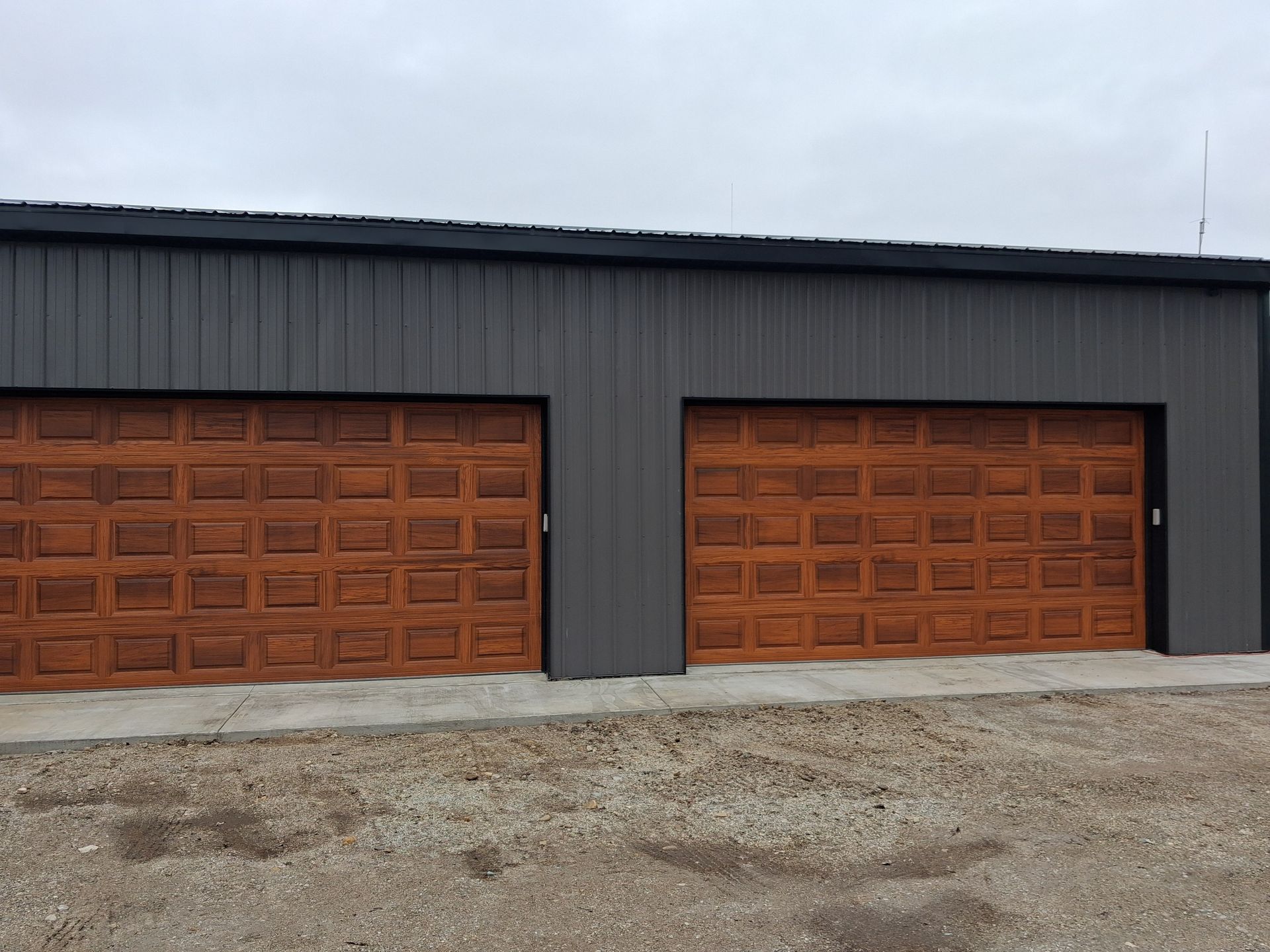 Two wooden garage doors on a gray metal building with a gravel driveway in front