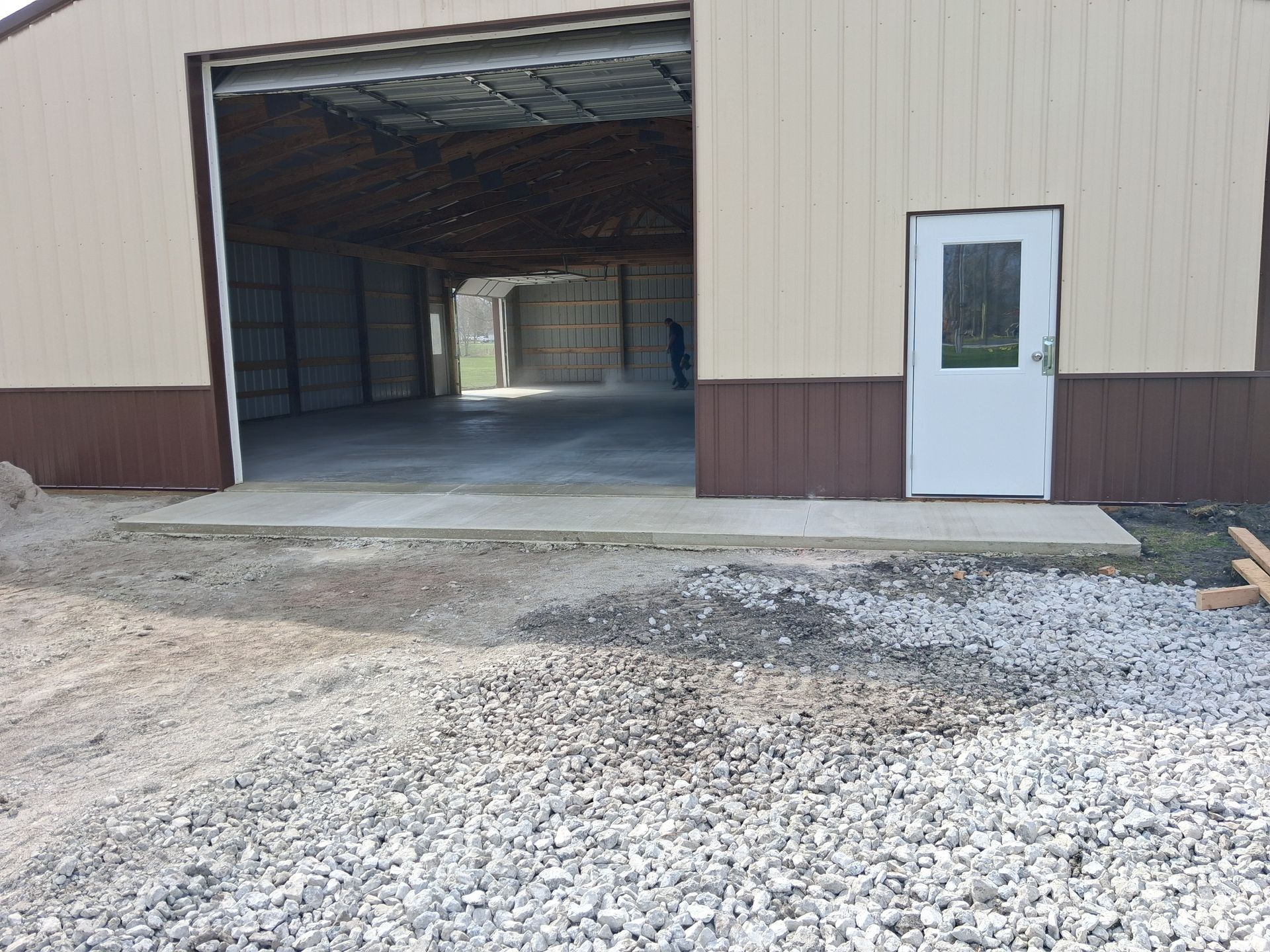 Open warehouse bay with gravel lot and white side door on tan and brown building