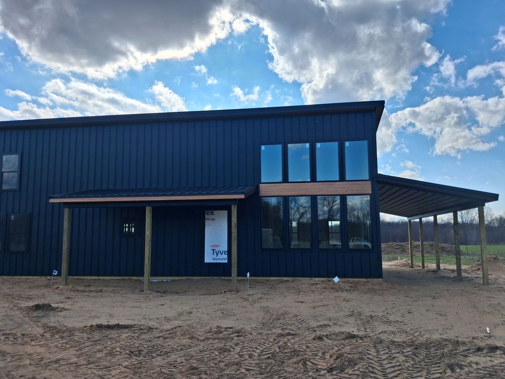 Blue metal building with a covered porch and large windows under a partly cloudy sky