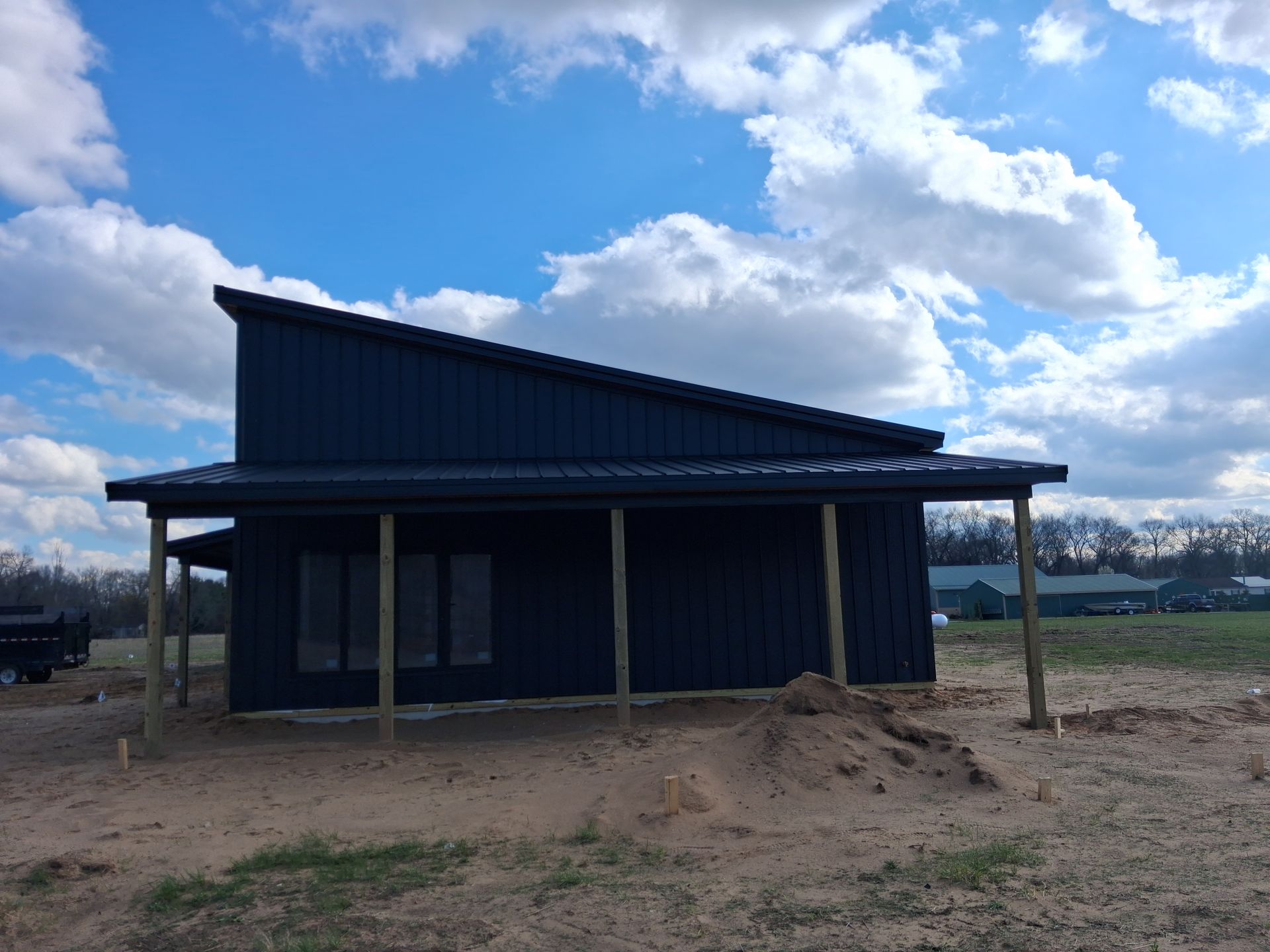 Small dark blue house under construction on a dirt lot beneath a cloudy sky.