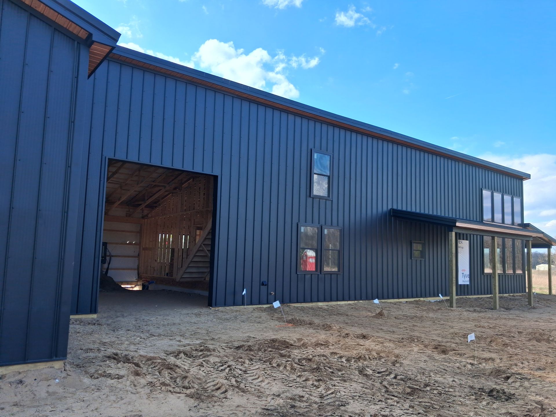 Blue metal barn with large open doorway and small porch on a dirt lot under a blue sky