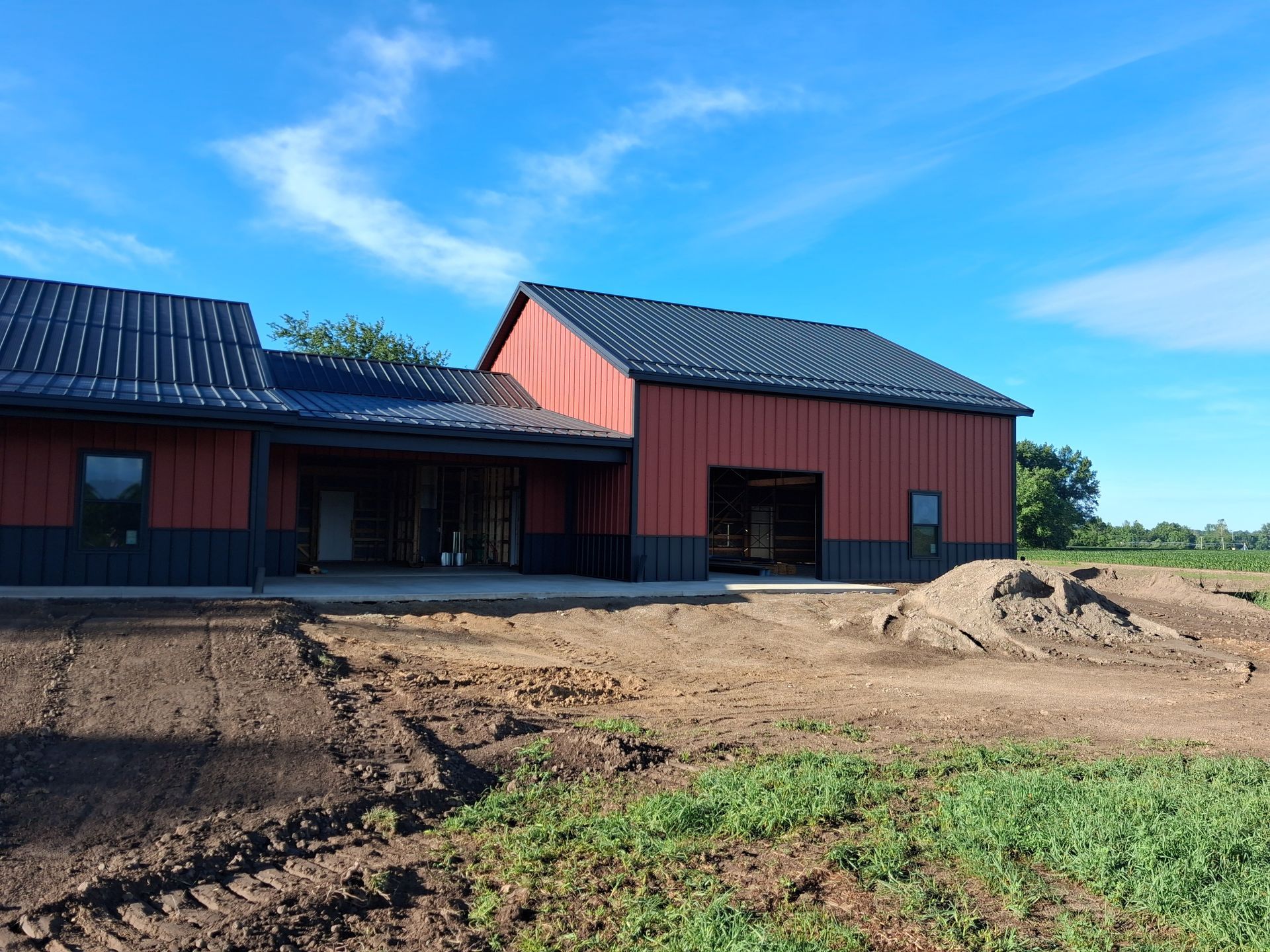 Red barn-style building with black roofs on a dirt lot under a blue sky