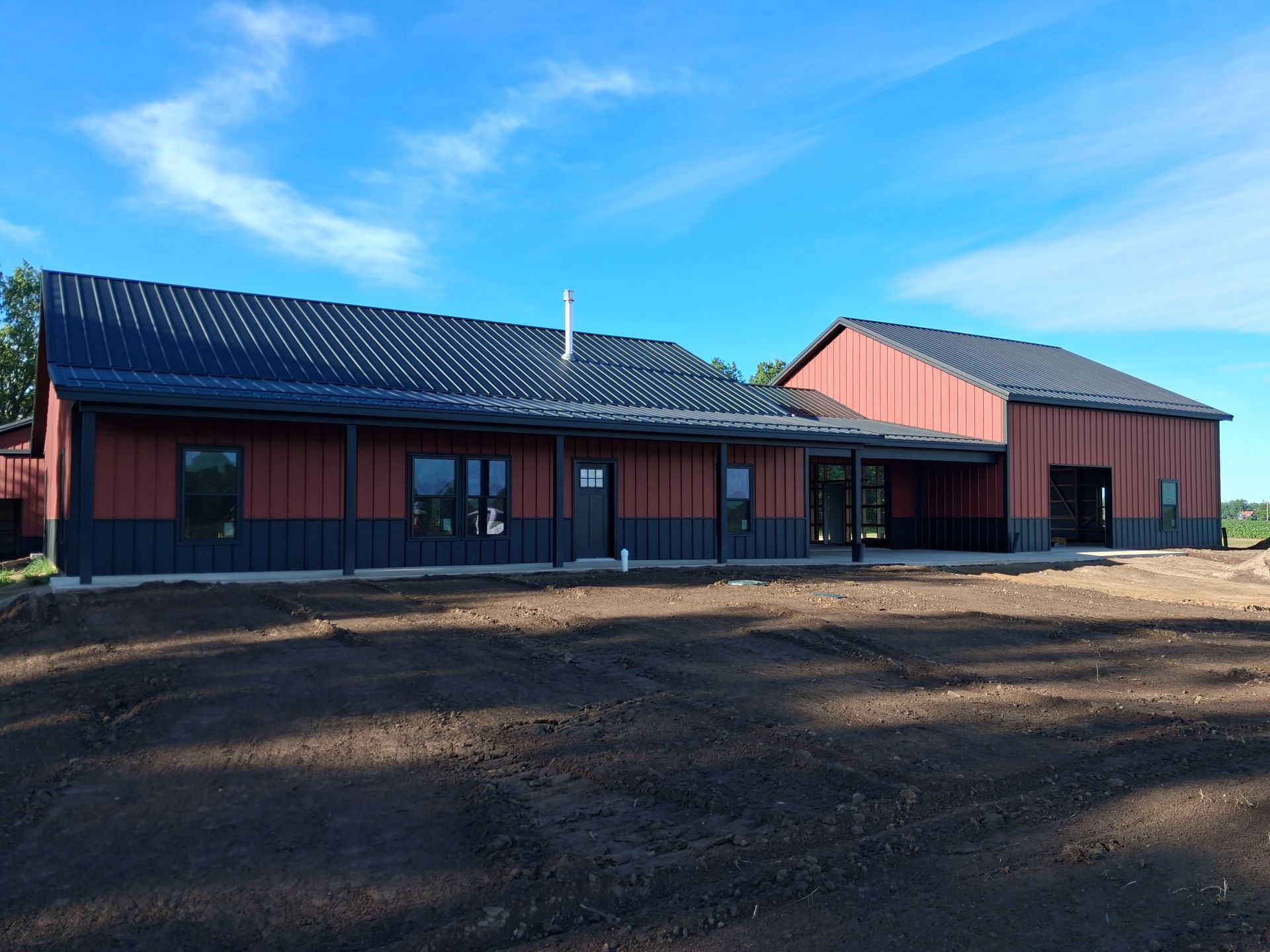 Single-story red building with dark roof on a dirt lot under a blue sky