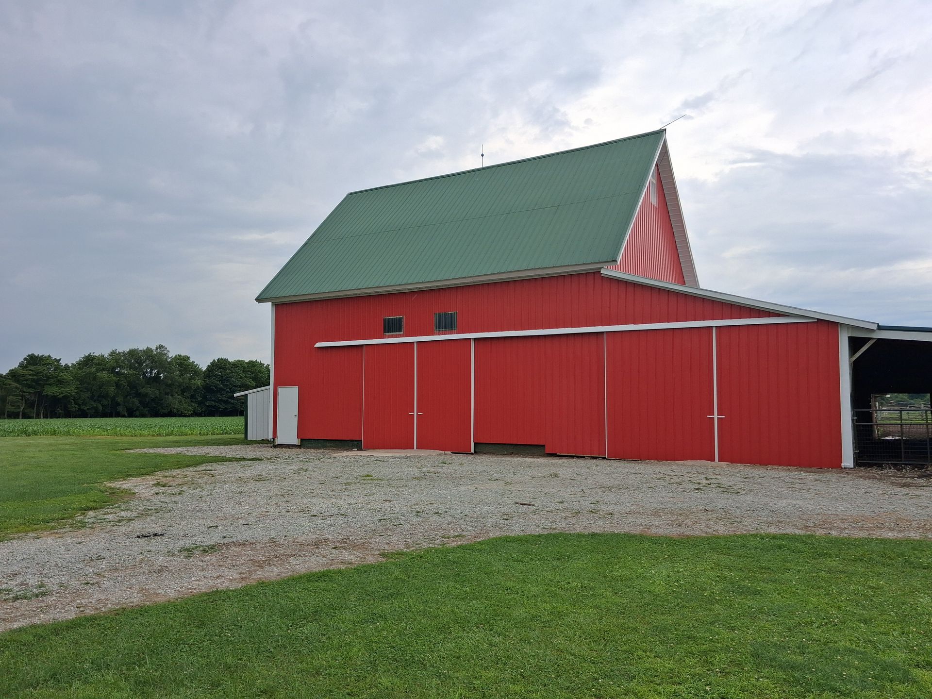 Red barn with green roof on a gravel drive beside grassy fields under a cloudy sky