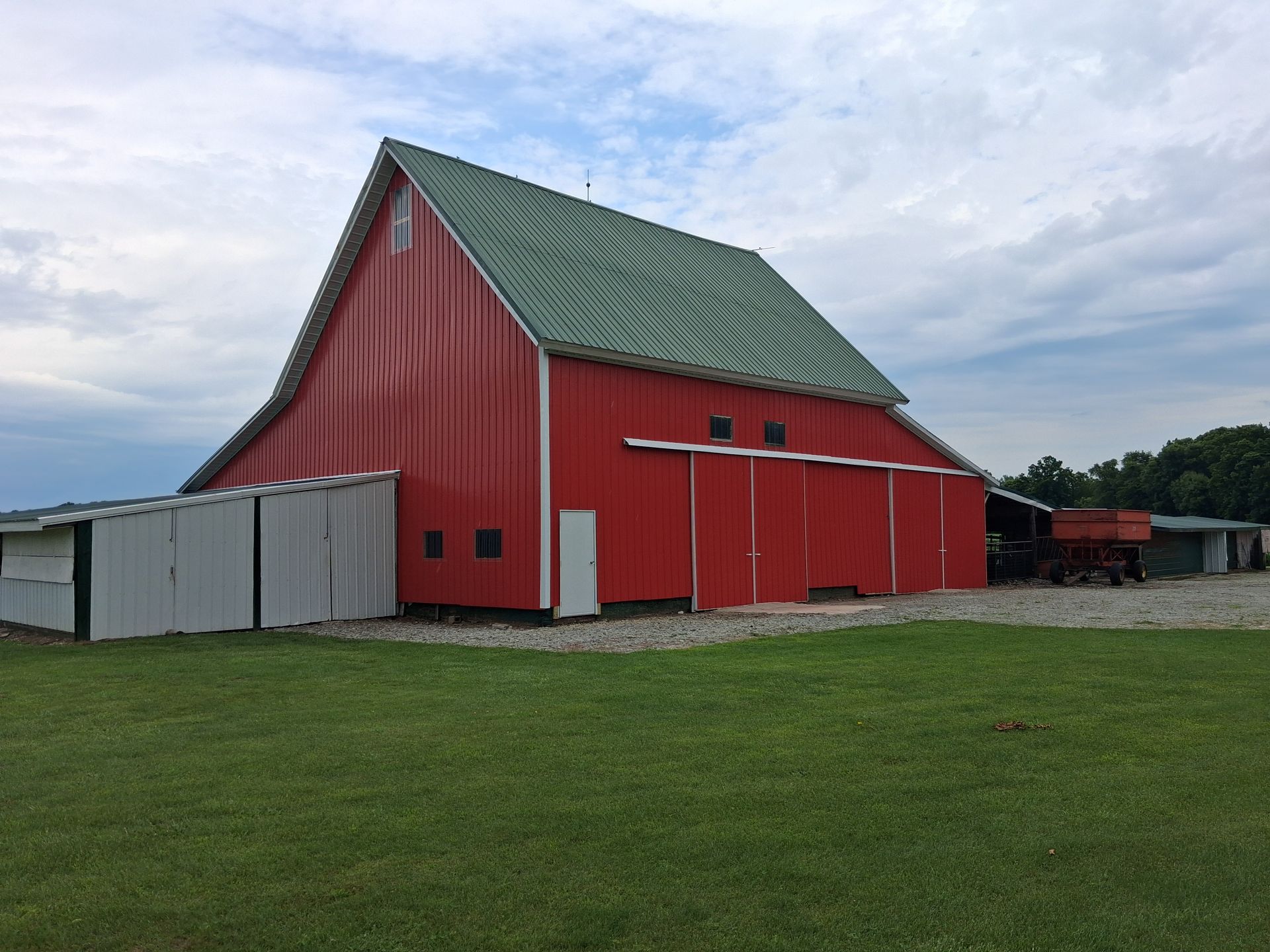 Red barn with green roof beside a fenced grassy field under a cloudy sky