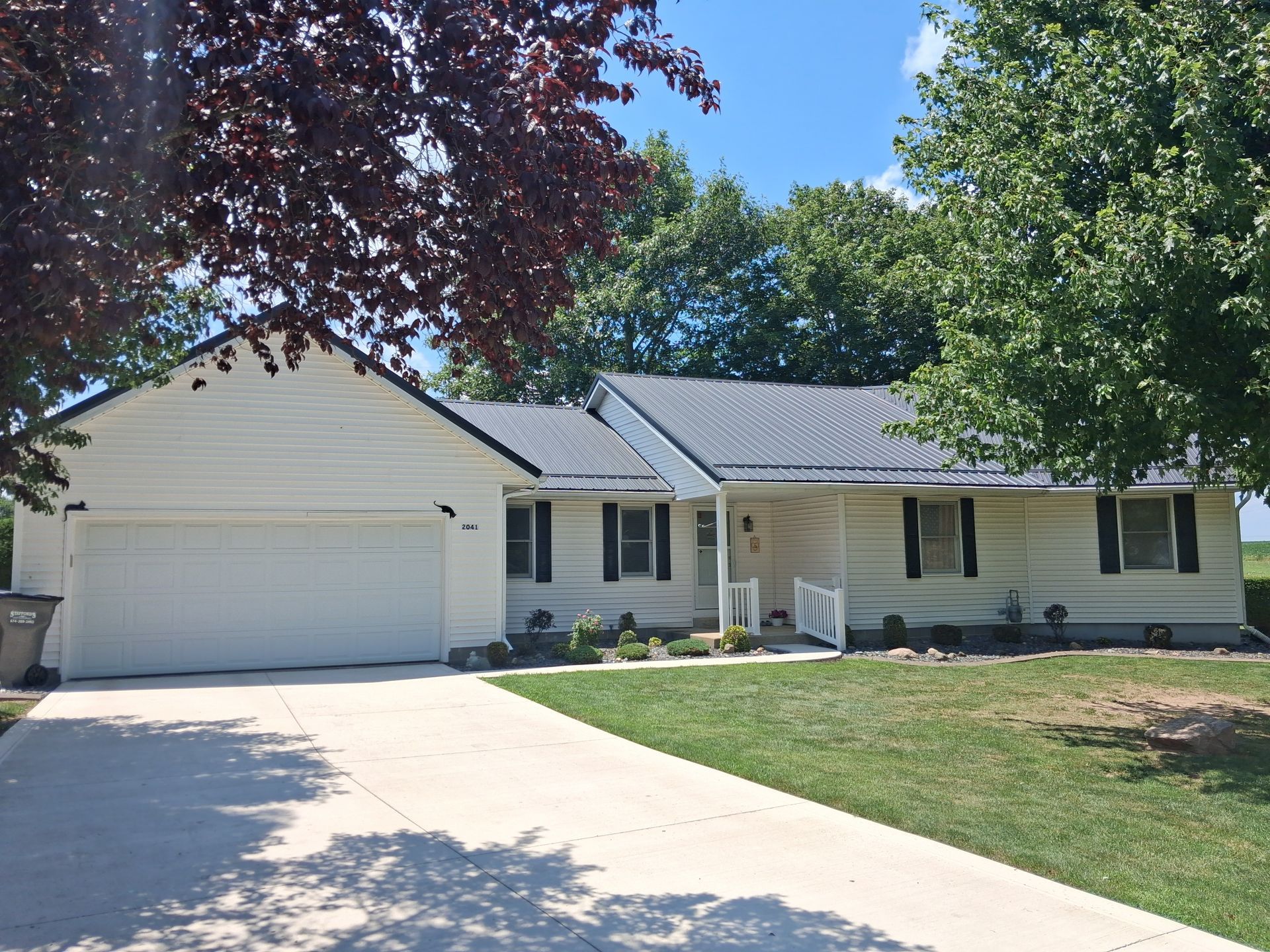 Suburban white house with two-car garage, front porch, and a curved driveway under trees