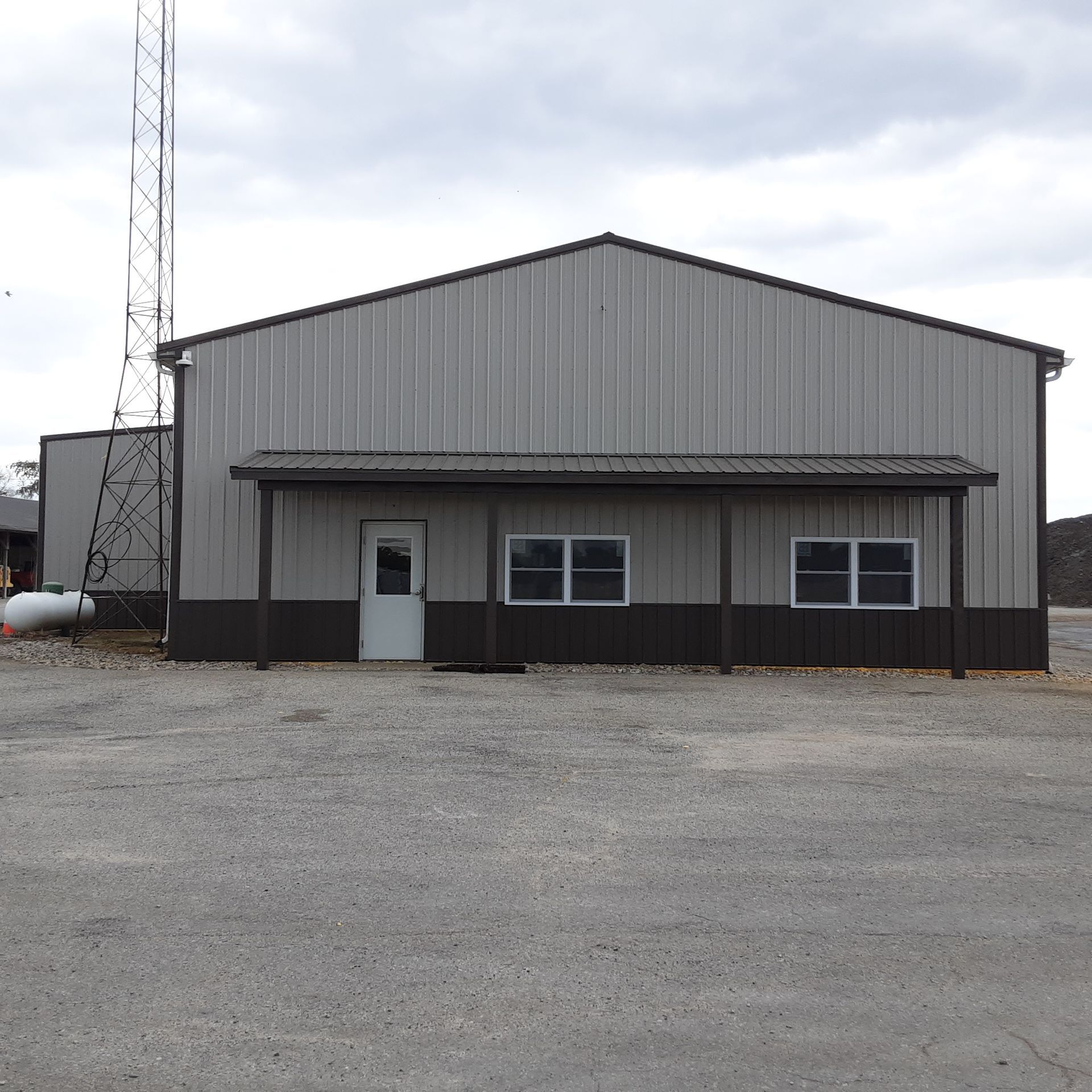 Front view of a gray metal warehouse with a white door, windows, and a radio tower beside it.