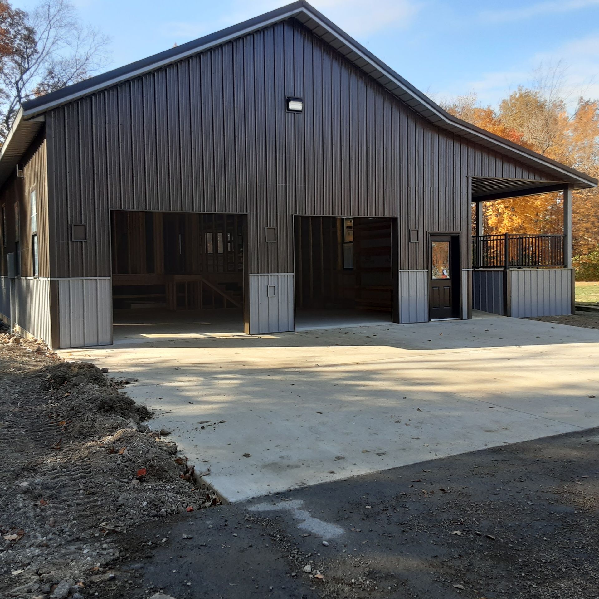 Dark metal barn-style building with three open bays and a concrete driveway in front