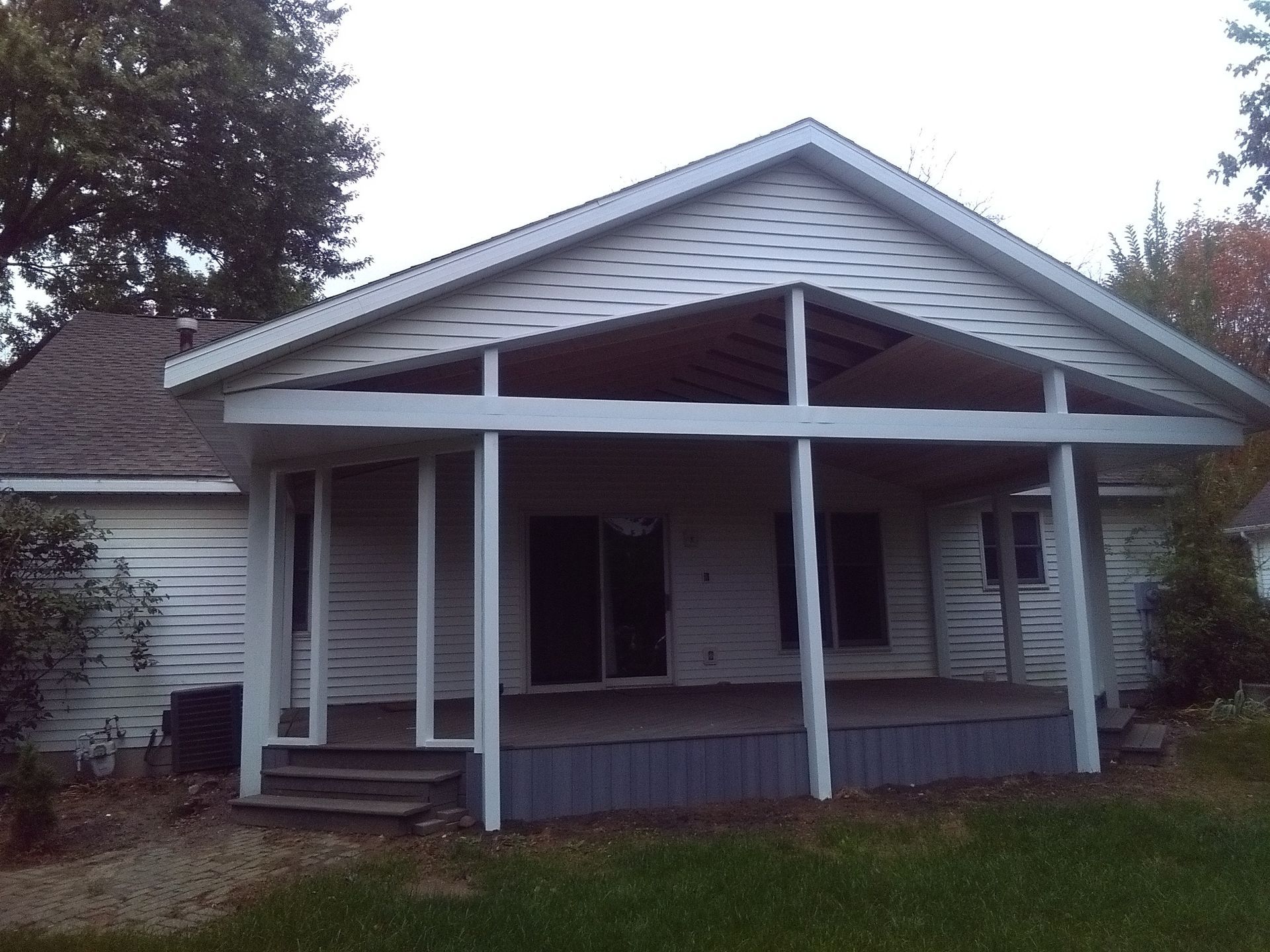 Small white house with a covered front porch and steps, surrounded by trees and grass.