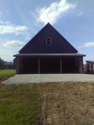Front view of a dark-roofed house with a wide porch and gravel driveway under a cloudy sky