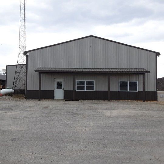 Gray metal warehouse building with a white door, dark trim, and a communications tower beside it