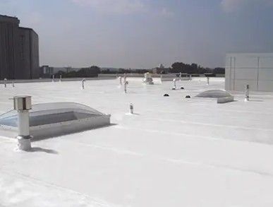 White flat rooftop with vents and skylights under a clear sky, with buildings in the distance