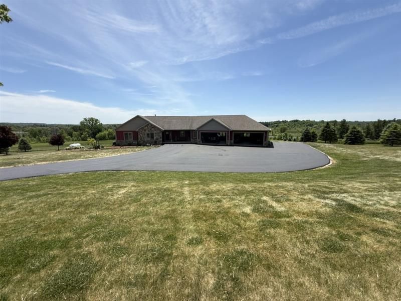 Single-story house with a wide gravel driveway and grassy front yard under a blue sky