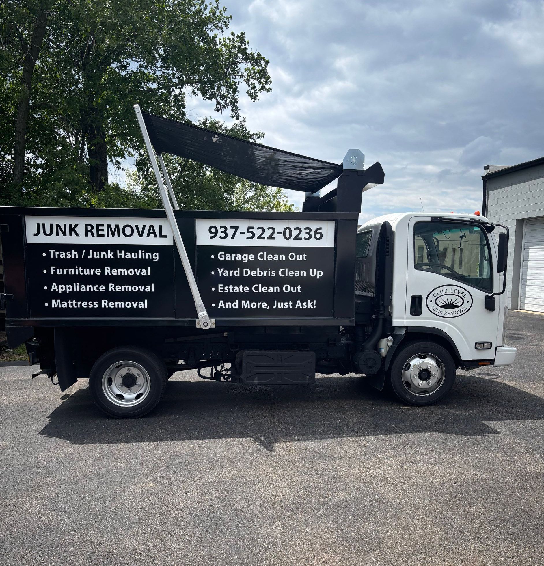 Black junk removal truck with service list parked outdoors under cloudy sky.